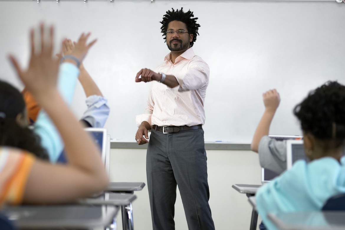 Male teacher standing before students (8-10) with hands raised